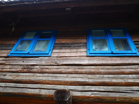 Ethno windows with a blue wooden frame. Vintage house exterior. Architectural complex Stanisici. Log cabin. Izba building in rural wooded area on the territory of the settlement of the Eastern Slavs
