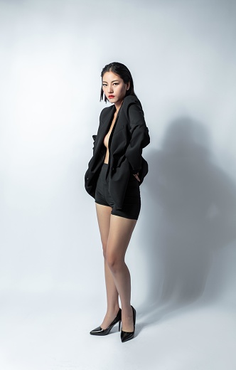 Asian woman in black suit and high heels posing on white background