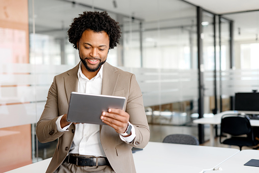 African-American young businessman looking at his tablet with an expression of pleasant surprise. This shot perfect for conveying concepts like real-time data analysis, business agility, e-commerce