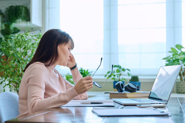 istock Tired sad mature woman at workplace at table with computer laptop 1955367334