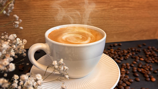 A cup of cappuccino on a dark background, next to a gypsophila flower. Background with the theme of coffee, cafe with steam on a black background.