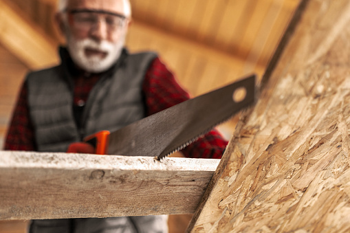 Senior male craftsman at his workshop sawing wood