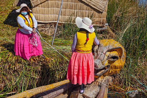Uros, Peru - April 29, 2022: women in traditional dresses near house on the floating Uros Islands on Lake Titicaca in Peru.