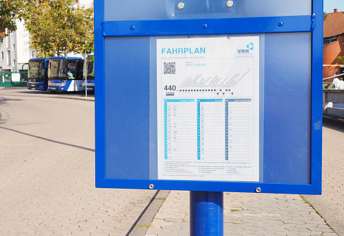 Bad Kreuznach, Germany – September 30, 2023: close-up timetable, blue, white, outside, buses parking background, departure times, stop names, direction Alzey, line 440, VRN, sunny day,