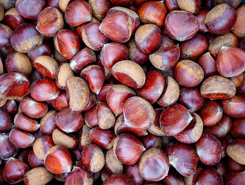 A container filled with shiny freshly harvested sweet chestnuts on a market stall.