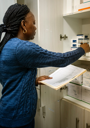 Female pharmacist counting boxes of medication stored in a cabinet while taking inventory in a pharmacy