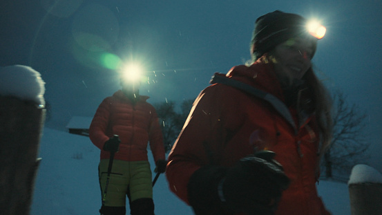 Young couple leave mountain hut with headlamps at night in the snow
