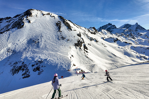 Family of three skis down slope at ski resort, snowcapped mountains in distance