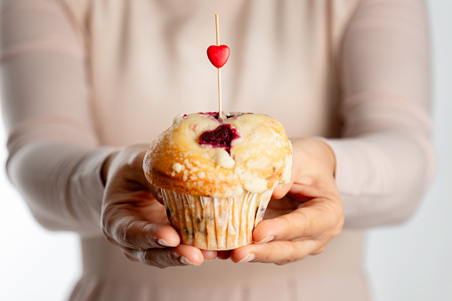 Unrecognizable female is holding a muffin with one stick and a small red heart shape on it.