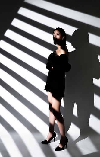Fashion model in a black dress posing in front of a striped background