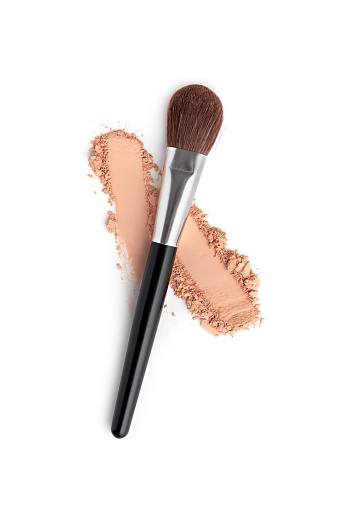 Makeup brush and crushed beige foundation for applying face powder isolated on white background