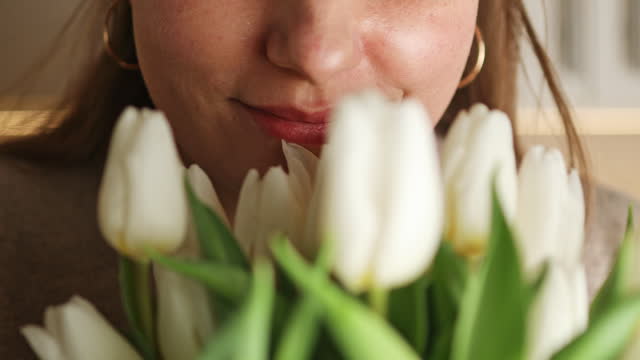 4k Close up of happy woman enjoy bouquet of white tulips. Housewife enjoying a bunch of flowers and interior of kitchen.