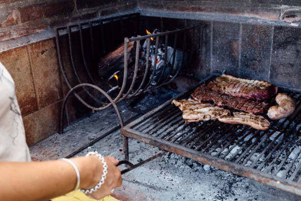 Woman making a barbecue. She is adding embers under the meat.