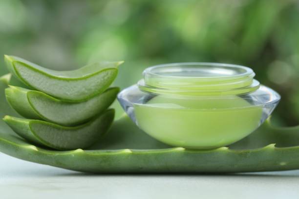 istock Jar with cream and cut aloe leaf on white table against blurred green background, closeup 1955625664