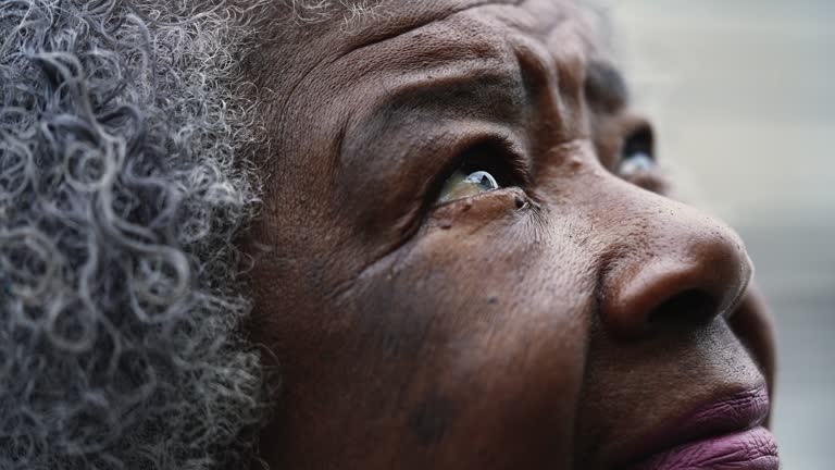 Grateful Senior African American woman macro close-up eyes and face gazing upwards at sky with FAITH and HOPE. closing and opening eyes in meditative PRAYER