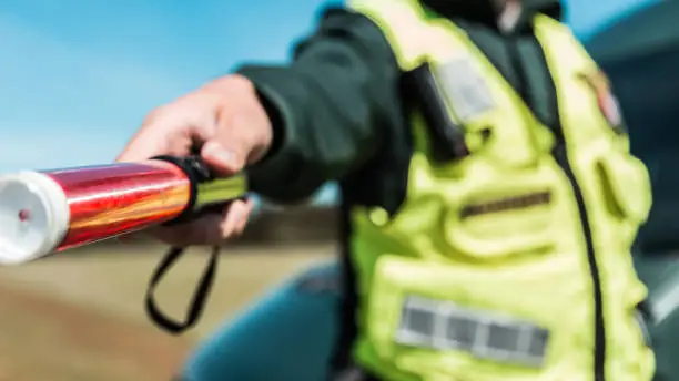 Traffic officer in high-visibility vest holding a baton for road control near a patrol vehicle, with safety equipment