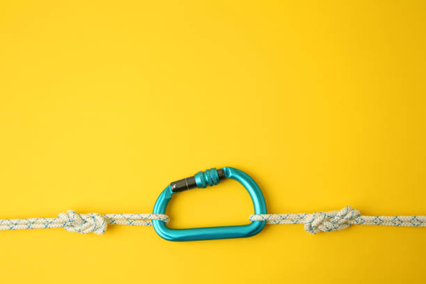 istock One metal carabiner with ropes on yellow background, top view. Space for text 1955658307