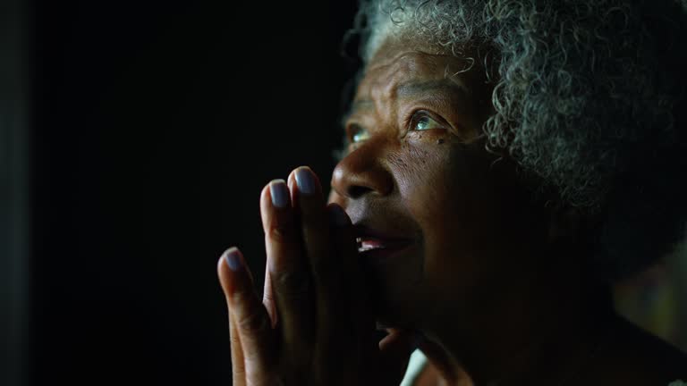 Faithful and Spiritual Senior African American woman with gray hair opening eyes feeling GRATEFUL while PRAYING to GOD. One religious elderly lady in 80s close-up face