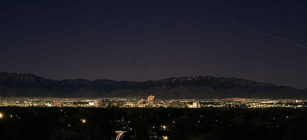 The night lights of Albuquerque, NM are bright and a contrast to the dark sky and the silhouette of the Sandia Mountains in the background.