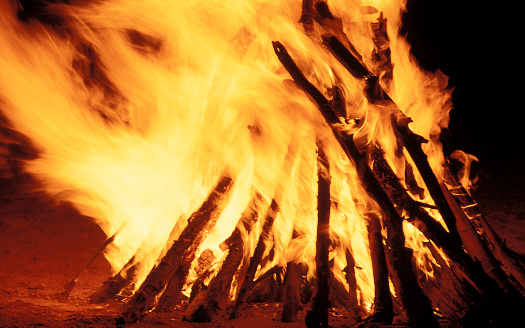 A large bonfire is burning wood timber at a Native American ceremony.