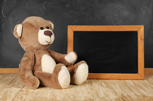 Teddy bear and small blackboard on wooden table. Space for text