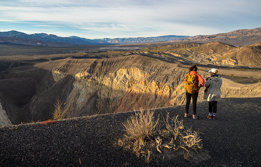 Two young women on a stunning journey under the vast desert sky, through the landscape of Ubehebe Volcanic field in Death Valley National Park, standing on a cliff of vulcanic crater