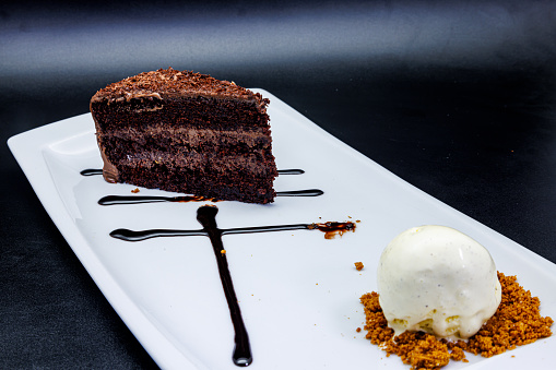 Composition of a Chocolate cake on a white plate with ice cream on a black background