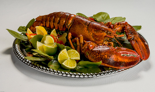 A steamed whole lobster served on a silver platter with fresh lemons and limes is certainly a gourmet meal for seafood lovers.