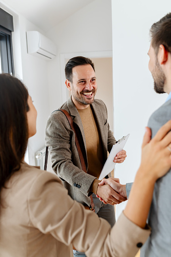 A young, beautiful, cheerful couple expecting a baby, talking with a real-estate agent visiting an apartment for sale or for rent. Future parents buying an apartment. Real estate concept. A new beginning