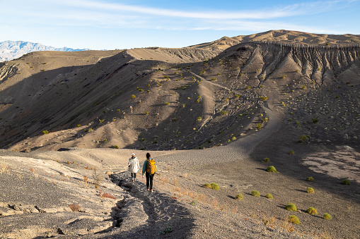 Two young women on a stunning journey under the vast desert sky, through the landscape of Ubehebe Volcanic Crater in Death Valley National Park, walking across a vast volcanic field