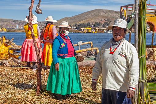 Uros, Peru - April 29, 2022: woman in traditional clothes rowing a uros totora boat near Uros Islands on Lake Titicaca in Peru.