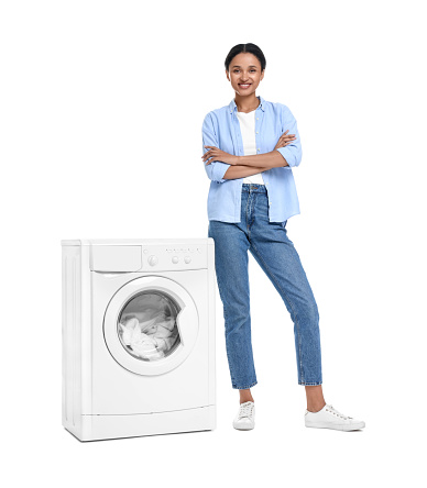 Beautiful woman near washing machine with laundry on white background