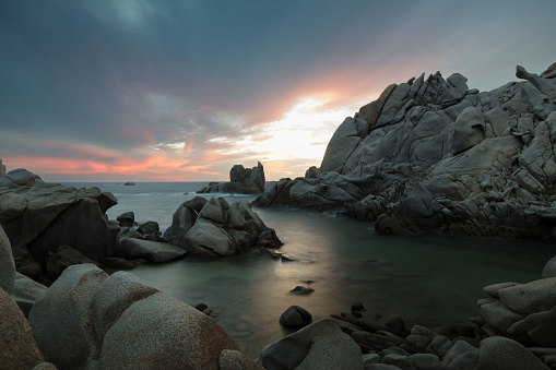 On the headland formed by giant granite boulders and overlooking the Strait of Bonifacio, the sunset is dramatic. The cloudy, sanguine sky is mirrored in the green waters of Cala Francese beach, already shrouded in dark, mysterious shadows.