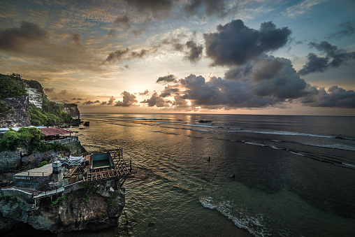 From the precipice of Bali's cliffs, behold an enchanting view that encompasses the boundless ocean, the serene skies, and a captivating sunset painted in tranquil tones.