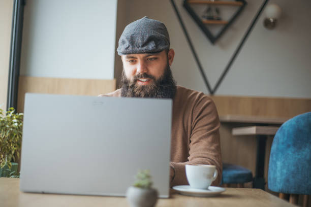 istock A bearded man is sitting in a cafe and using a laptop 1955808043