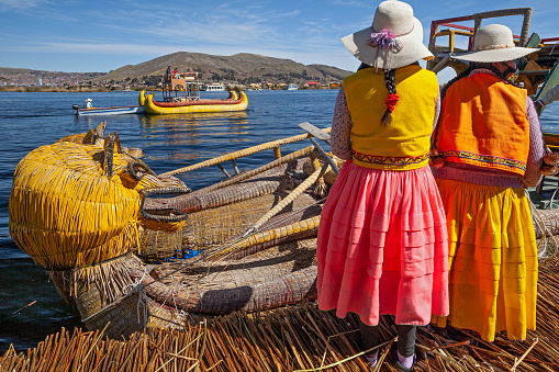 Uros, Peru - April 29, 2022: woman in traditional clothes rowing a uros totora boat near Uros Islands on Lake Titicaca in Peru.