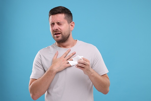 Man suffering from allergy on light blue background