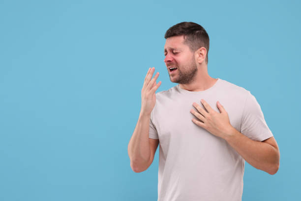 istock Allergy symptom. Man sneezing on light blue background. Space for text 1955829233
