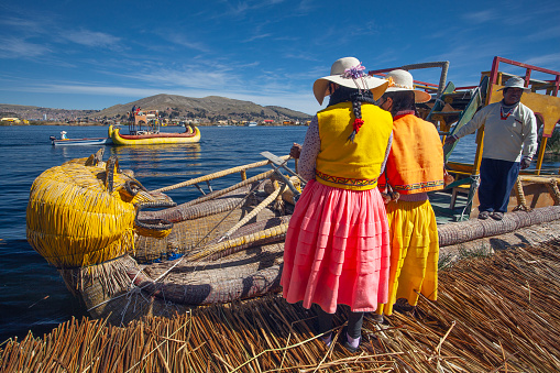 Uros, Peru - April 29, 2022: woman in traditional clothes rowing a uros totora boat near Uros Islands on Lake Titicaca in Peru.