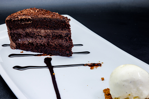 Composition of a Chocolate cake on a white plate with ice cream on a black background
