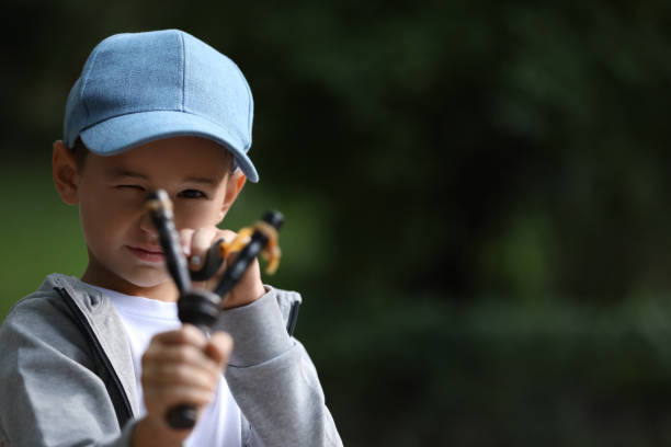 istock Little boy playing with slingshot outdoors. Space for text 1955841452