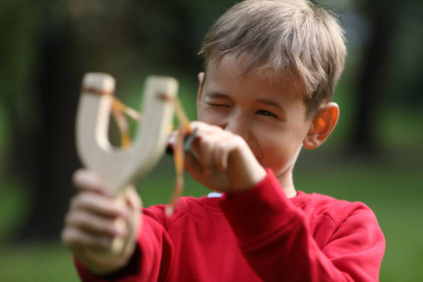 istock Little boy playing with slingshot in park 1955844076