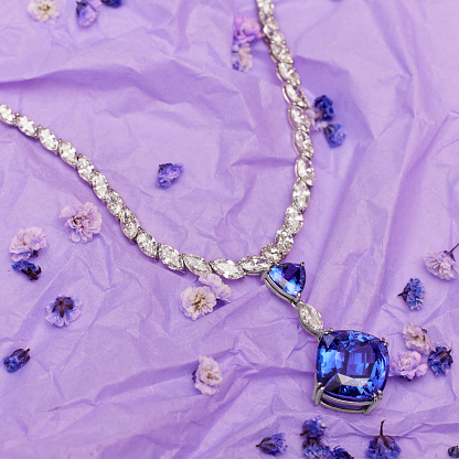 A beautifully crafted necklace with a shimmering blue stone, set against a vibrant purple background.