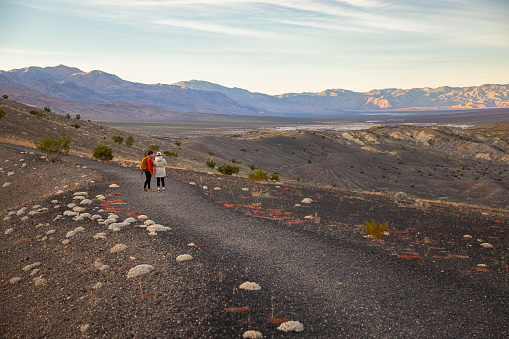 Two young women on a stunning journey under the vast desert sky, through the landscape of Ubehebe Volcanic Crater in Death Valley National Park, walking across a vast volcanic field
