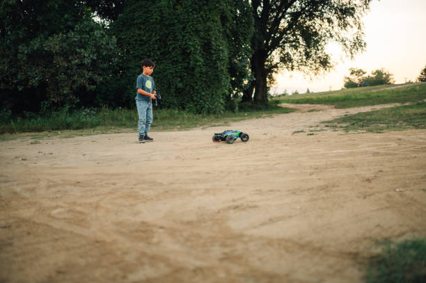 istock Boy running his electric toy car with a remote controller on a dirt road 1955876589