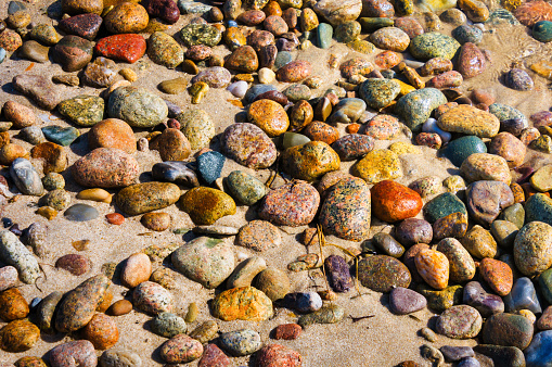 Seawater splashes over smooth, colorful granite stones on a Cape Cod beach.  These stones were deposited on the beach at the end of the last ice age eons ago.