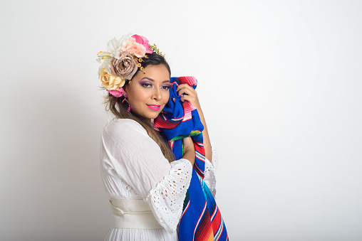 Mexican woman with flower headdress holding colorful serape. White background.