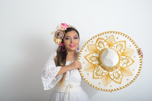 Mexican woman with flower headdress holding a mariachi hat. Woman with sombrero, white background.
