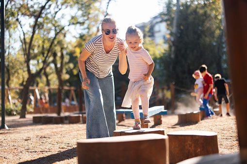 A smiling Caucasian child having fun in the park with her mother.
