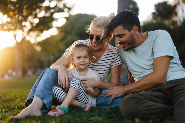 A Happy Beautiful Family Of Three Enjoying Spending Their Leisure Time Together A smiling Caucasian family sitting on the grass in the park and relaxing on a sunny day. couple hope sky blue stock pictures, royalty-free photos & images
